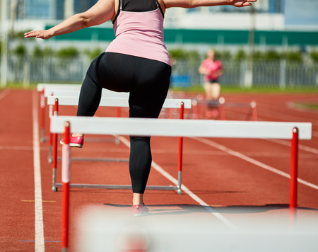 Woman mid-stride jumping over a hurdle on a track, symbolizing the personal journey of overcoming addiction through hypnotherapy.